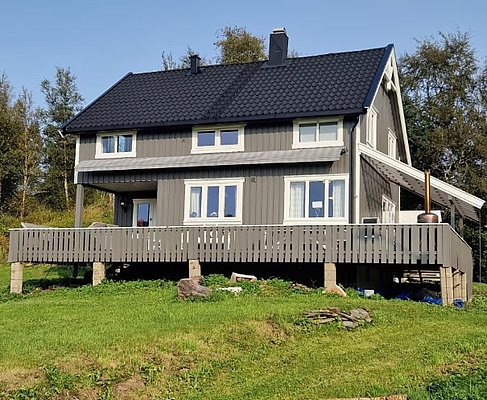 Gemütliches graues Holzhaus in Nordland, Norwegen, mit großer Terrasse, umgeben von grüner Landschaft. Perfekt für Angelurlaube und Entspannung in der Natur. Ideal für Erholungssuchende und Abenteuerlustige.