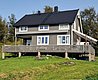 Gemütliches graues Holzhaus in Nordland, Norwegen, mit großer Terrasse, umgeben von grüner Landschaft. Perfekt für Angelurlaube und Entspannung in der Natur. Ideal für Erholungssuchende und Abenteuerlustige.