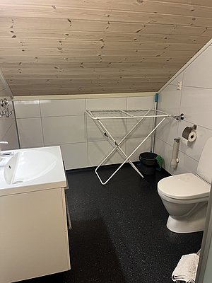 Modernes Badezimmer in Nord-Norwegen mit weißem Waschbecken, Toilette, Wandpaneelen und kleinem Wäscheständer. Praktisch und gemütlich, ideal für Angelreisen in arktischer Umgebung. Barrierefreier Zugang für alle Abenteurer.