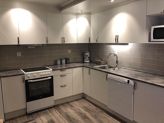 Moderne Küche in Nord-Norwegen mit weißer Ausstattung und grauen Fliesen. Ausgestattet mit Herd, Spülbecken, Spülmaschine und Mikrowelle. Perfekt für einen komfortablen Angelurlaub mit Kochmöglichkeiten in malerischer Umgebung.