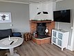 Ein gemütliches Wohnzimmer mit einem Holzofen in einer Backsteinecke, einem weißen Couchtisch mit einer Kerze, einem Sofa, einem Holzstapel und einem Flachbildfernseher an der Wand.