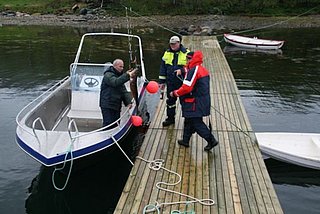 Drei Angler auf einem Steg in Nord-Norwegen begutachten freudig ihren Fang neben einem Boot. Perfekt für Angelreisen und Meeresangeln in spektakulärer Landschaft.