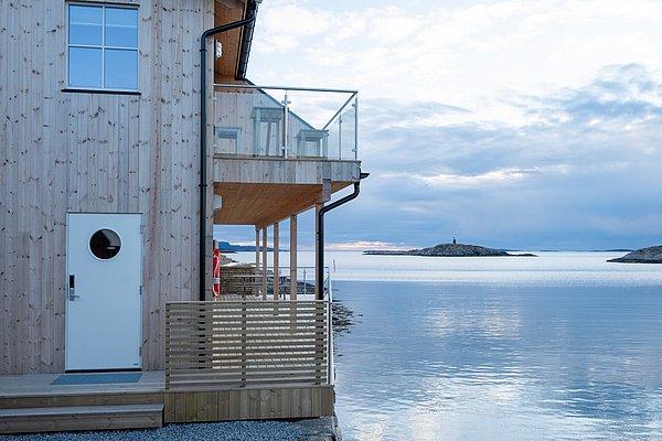 Modernes Holzhaus am ruhigen Fjord in Hitra, Norwegen. Glasbalkon mit Blick auf malerische Inseln. Ideal für Entspannung und Angelabenteuer in skandinavischer Natur. Perfekte Kulisse für Angelreisen und unvergessliche Erlebnisse.