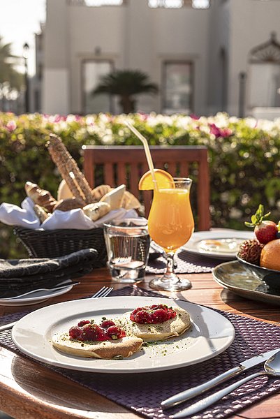 Frühstück im Freien mit Pfannkuchen und Erdbeeren, Saft im Glas, im sonnigen Garten einer süd-norwegischen Unterkunft. Entspanntes Ambiente für kulinarischen Genuss in der Natur.