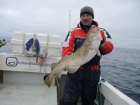 Ein Angler in einem Boot hält stolz einen großen Kabeljau, aufgenommen bei einer Angelreise in Island.