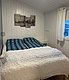 Gemütliches Schlafzimmer in Hitra, Norwegen: Doppelbett mit blau-grüner Bettwäsche, weiß getäfelte Wände, großes Fenster mit Vorhang. Perfekt für Erholung im Angelurlaub. Wandbild mit Brückenmotiv dekoriert den Raum.