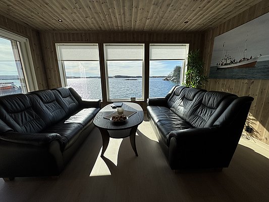 Gemütliches Wohnzimmer mit Panoramablick auf das Meer bei Hitra, Norwegen. Moderne Ledersofas, Holzwände und große Fenster schaffen eine einladende Atmosphäre zum Entspannen und Natur genießen. Perfekt für Angelurlaub und Erholung in skandinavischer Idylle.