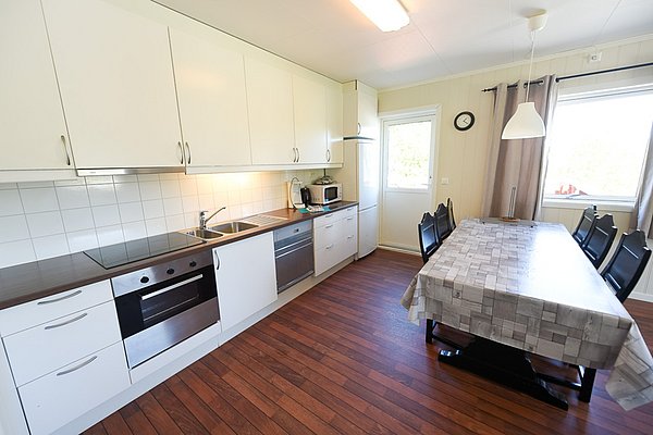 Moderne Küche in Hitra, Norwegen: helle Schränke, Holzoptik-Boden, Esstisch mit Platz für sechs Personen. Ideal für Angelreisende, die Komfort und Funktionalität suchen. Perfekte Unterkunft für entspannte Abende nach einem fischreichen Tag.