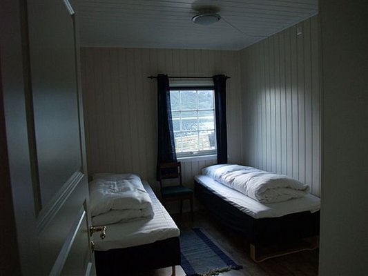 Gemütliches Schlafzimmer in Nordland, Norwegen. Zwei Einzelbetten, Holzwände und Fenster mit Blick auf Fjordlandschaft bieten perfekte Erholung nach einem Tag voller Abenteuer und Angeln. Ideal für Naturliebhaber und Erholungssuchende.
