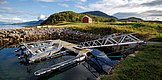 Nord-Norwegen: Malerische Küstenlandschaft mit klaren Gewässern und Booten an einem Steg, umgeben von grünen Hügeln und einem roten Hütte. Perfekte Kulisse für Angelreisen und Outdoor-Abenteuer.