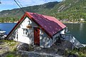 Gemütliche Hütte am Fjord auf Hitra, Norwegen, ideal für Angelreisen. Die Terrasse bietet Blick auf das glitzernde Wasser und die bewaldeten Hügel. Perfekter Ausgangspunkt für Meeresangeln und Erholung in unberührter Natur.