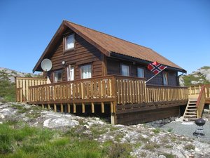 Holzhütte in Hitra, Norwegen: Idyllische Lage in felsiger Landschaft, umgeben von Natur. Perfekt für Angelurlaub mit schöner Aussicht, norwegischer Flagge und Sonnenterrasse. Ideal für Erholung und Abenteuer. Klarer Himmel und ruhige Umgebung.