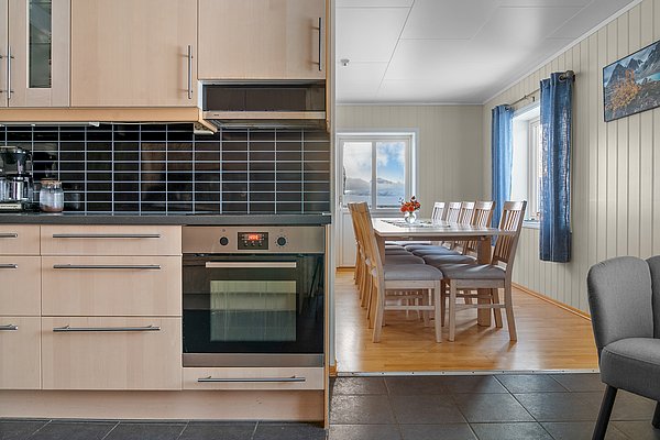 Moderne Küche in Nordnorwegen mit Holzschränken, schwarzen Fliesen und Essbereich. Der Raum bietet Blick auf die winterliche Landschaft durch große Fenster, ideal für gemütliche Angelurlaube.