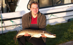 Ein Mann hält einen großen Hecht vor einem Boot.