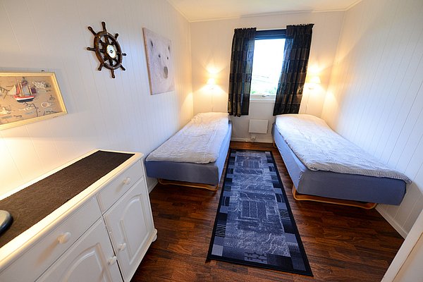 Gemütliches Schlafzimmer in Nord-Norwegen mit zwei Einzelbetten, heller Dekoration und maritimen Elementen. Perfekte Unterkunft für Angelreisen in der arktischen Region, umgeben von beeindruckender Natur. Ideal für Erholung nach einem erfolgreichen Angeltag.