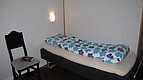 Ein gemütliches Einzelzimmer in Hitra, Norwegen: Bett mit bunter Blumenbettwäsche, Wandlampe, schwarzer Stuhl, ideale Unterkunft für Angelurlaub und Entspannung in skandinavischer Umgebung.