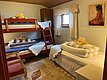 Gemütliches Schlafzimmer in Hitra, Norwegen, mit Etagenbett und Einzelbett. Ideal für Angelurlauber, bietet es eine komfortable Erholung nach einem langen Tag am Meer. Warme Holzelemente und frische Handtücher inklusive.