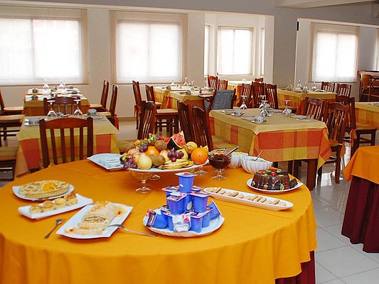 Ein Buffet-Tisch mit verschiedenen Frühstücksoptionen wie Joghurt, Gebäck, Obst und Pudding vor einem einladend gedeckten Speiseraum mit karierten Tischdecken. Ein Buffet-Tisch mit verschiedenen Frühstücksoptionen wie Joghurt, Gebäck, Obst und Pudding vor einem einladend gedeckten Speiseraum mit karierten Tischdecken.