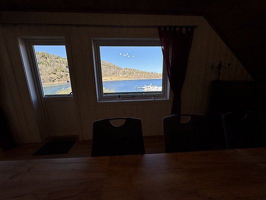 Blick aus einem gemütlichen Raum in Hitra, Norwegen, auf eine malerische Küstenlandschaft mit ruhigem Wasser und bewaldeten Hügeln. Perfekter Ausgangspunkt für Angelreisen und Naturerlebnisse.