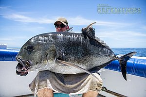 Ein Angler hält einen beeindruckenden Giant Trevally auf einem Boot vor der Küste von Malindi, Kenia. Perfekter Angelurlaub mit Sportfischen und atemberaubendem Meerblick. Ideal für Abenteuerlustige und Meeresangler.