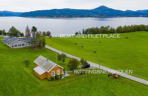 Norwegische Landschaft auf Hitra: Weite grüne Wiesen, Viehweiden, ein gelbes Haus und ein Bootsanleger am ruhigen Meer. Perfekt für entspannte Angelerlebnisse, umgeben von beeindruckender Natur.