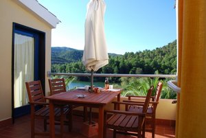Gemütliche Terrasse mit Holzmöbeln in Riba Roja, Spanien. Im Hintergrund grüner Wald und blauer Himmel. Ideal für entspannende Angelreisen. Ausstattung mit Sonnenschirm, perfekter Blick auf Natur und Landschaft.
