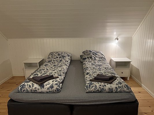 Gemütliches Schlafzimmer in Nord-Norwegen: Helles, schlichtes Design mit zwei Einzelbetten, weißer Holzverkleidung und Nachttischen. Perfekt für erholsame Nächte nach abenteuerlichen Angelausflügen. Ideal für einen erholsamen Angelurlaub im hohen Norden.
