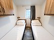 In einer gemütlichen Hütte in Nord-Norwegen befinden sich zwei Einzelbetten in einem hellen Schlafzimmer mit Holzschränken und einem kleinen Fenster. Ideal für Angelreisende.