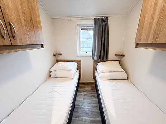 In einer gemütlichen Hütte in Nord-Norwegen befinden sich zwei Einzelbetten in einem hellen Schlafzimmer mit Holzschränken und einem kleinen Fenster. Ideal für Angelreisende.