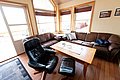 Gemütliches Wohnzimmer mit Ledersofas und Sesseln in einer Ferienhütte in Südwest-Norwegen. Helle Holzverkleidung und große Fenster bieten Blick ins Freie. Ideal für Angelreisen und Entspannung nach einem erfolgreichen Fang.