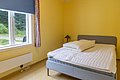 Gemütliches Schlafzimmer in Hitra, Norwegen, mit einem großen Bett und gelben Wänden. Ein Fenster bietet Blick ins Grüne, ideal für ruhige Nächte nach aufregenden Angelabenteuern. Perfekte Unterkunft für entspannte Angelreisen.