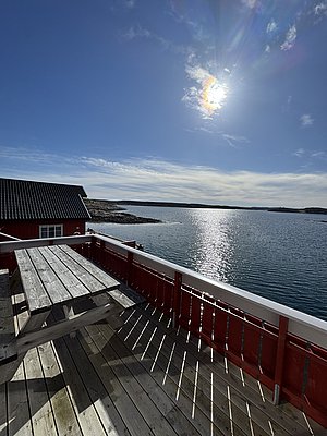 Sonnige Terrasse mit Blick auf das glitzernde Meer bei Hitra, Norwegen. Rote Holzhäuser strahlen skandinavisches Flair aus. Ideal für Angelurlaub und Naturliebhaber. Perfekte Kulisse für Erholung und Abenteuer.