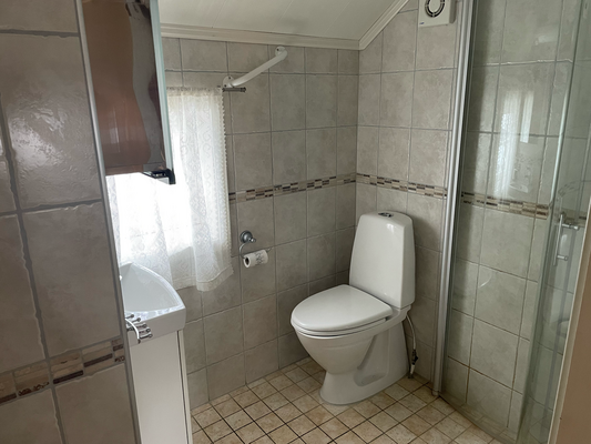 Helles, gefliestes Badezimmer in Nord-Norwegen mit Dusche, Toilette und Waschbecken. Ideal für gemütliche Angelurlaube. Barrierefrei, sauber und funktional gestaltet für Komfort nach einem langen Angeltag.