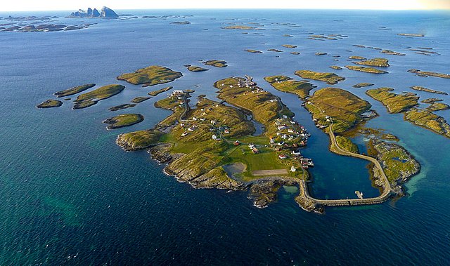 Luftaufnahme der Schärenlandschaft in Nordland, Norwegen. Kleine, grüne Inseln mit verstreuten Häusern, umgeben von blauem Meer. Malerische Küstenlinie, perfekt für Angelreisen. Ein idyllischer Rückzugsort für Naturliebhaber und Abenteurer.