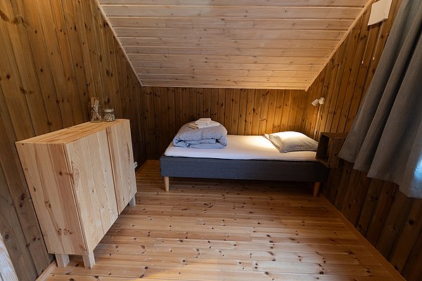 Gemütliches Schlafzimmer aus Holz in Nord-Norwegen, mit Einzelbett und minimalistischem Schrank, bietet eine warme und einladende Atmosphäre für naturnahe Erholung. Ideal für Angler und Reisende in skandinavischer Umgebung.
