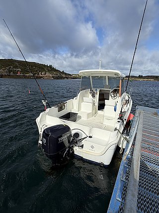 Kleines Angelboot in Süd-Norwegen am Steg, bereit für Meeresangeln. Bewölkter Himmel und felsige Küste im Hintergrund. Ideal für Angelreisen in Norwegen.