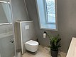 Modernes Badezimmer in Hitra, Norwegen, mit wandhängendem WC, großen Fenster für natürliches Licht, grauen Wänden und grüner Pflanze. Idealer Ausgangspunkt für Angelabenteuer und entspannte Erholung in skandinavischem Design.