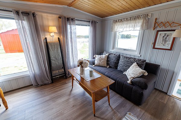 Gemütliches Wohnzimmer einer norwegischen Angelhütte in Hitra. Helle Fenster mit Blick auf die Natur, stilvolle Holzmöbel und eine komfortable Couch laden zum Entspannen nach einem erfolgreichen Angeltag ein. Ideal für Angelreisen.