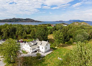 Die idyllische Landschaft von Hitra, Norwegen, zeigt ein charmantes weißes Haus umgeben von grünen Wäldern und dem blauen Meer im Hintergrund – ideal für entspannte Angelreisen und Naturerlebnisse.