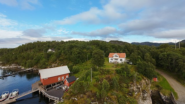 Küste von Hitra, Norwegen: Rotes Bootshaus am Wasser, umgeben von dichter grüner Natur. Perfekter Ort für Angelreisen und Erholung in skandinavischer Idylle. Abenteuer und Entspannung in beeindruckender Landschaft.