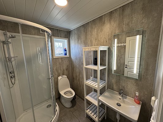 Modernes Badezimmer in Hitra, Norwegen: Duschecke, Toilette, Waschbecken und Regal, helle Holzdecken und graue Wände. Perfekt nach einem erholsamen Angeltag. Ideal für Angelreisen.