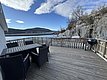 Eine sonnige Holzterrasse mit Essbereich und Grill bietet entspannte Aussicht auf Fjord und Berge in Hitra, Norwegen. Perfekt für einen Angelurlaub in idyllischer Umgebung.