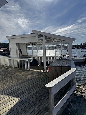 Eine weiße, überdachte Terrasse mit Holzsteg ragt über das Wasser in der malerischen Region Hitra, Norwegen. Perfekt für Angelurlaube und Naturerlebnisse. Ruhiger Ort mit atemberaubender Aussicht auf den Fjord.