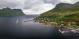 In Nord-Norwegen zeigt das Bild eine Küstenlandschaft auf der Insel Senja mit dramatischen Bergen, einem ruhigen Fjord und einem kleinen Hafen. Perfekt für Angelreisen und Naturerlebnisse. Bewölkter Himmel hebt die natürliche Schönheit hervor.