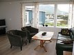 Gemütliches Wohnzimmer mit Blick auf einen norwegischen Fjord in Nordland. Helle Sitzecke, moderne Möbel, große Fenster und wunderschöner Ausblick auf Boote und Berge. Perfektes Angelreiseziel für Erholung und Abenteuer.