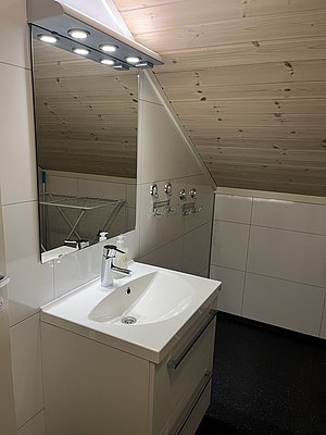 Ein modernes Badezimmer in Nord-Norwegen mit Holzdecke und beleuchtetem Spiegel. Das stilvolle Waschbecken sorgt für ein gemütliches Ambiente, perfekt für Erholung nach einem aufregenden Angeltag.