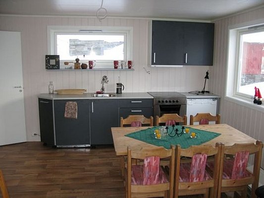 Gemütliche Küche in Nord-Norwegen: Moderne Ausstattung mit grauen Schränken, Esstisch für sechs Personen und viel Tageslicht durch große Fenster. Ideal für Anglerurlaub und kulinarische Erlebnisse in skandinavischer Umgebung.