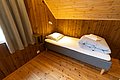 Gemütliches Schlafzimmer in Nordnorwegen mit Holzwänden und -decke, einem Einzelbett mit hellen Bettbezügen, Tageslicht von einem Fenster und Kuscheldecke. Ideal für Entspannung nach einem erlebnisreichen Angeltag.