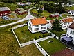 Charmantes Dorf in Nord-Norwegen: Traditionelle weiße Holzhäuser mit roten Dächern, umgeben von grünen Wiesen und Gärten. Malerische Landschaft mit blühenden Bäumen und ruhigen Straßen. Ideal für Angelurlauber und Naturliebhaber.