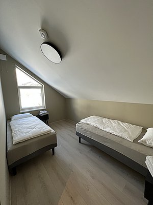Nordland, Norwegen: Gemütliches Zimmer mit zwei Einzelbetten, hellem Holzfußboden und schräger Decke. Ideal für erholsame Nächte nach einem erfolgreichen Angelausflug in der atemberaubenden Natur Norwegens. Perfekte Unterkunft für Angelreisende.